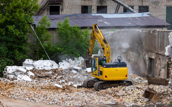 View of a yellow excavator demolishing an old brick building with debris and dust in a construction site Vilnius, Vilnius County, Lithuania.