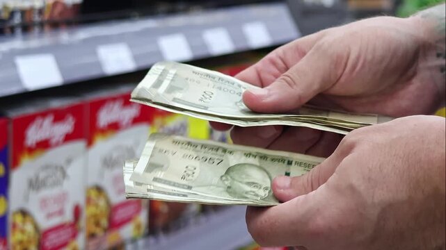Man counting 500 Indian rupee banknotes in a grocery store aisle. Close-up cash handling near supermarket shelves, consumer spending and retail purchase concept
