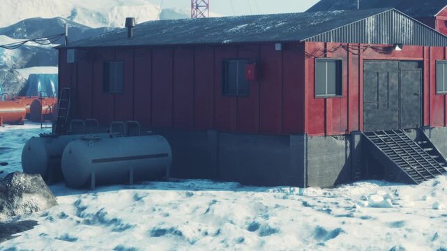 A red structure stands in a snowy area. The building has a flat roof and a set of stairs. Nearby, there are large patches of snow and some equipment used for research.
