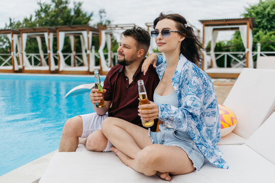 Young couple enjoying drinks by the swimming pool on a summer day. Concept vacation, relaxation and lifestyle.
