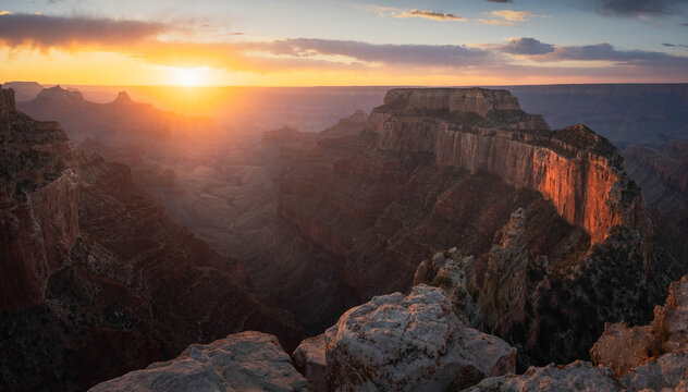 View of the Grand Canyon with its vast rocky cliffs illuminated by the golden light of a setting sun under a soft cloudy sky Coconino County, Arizona, United States.