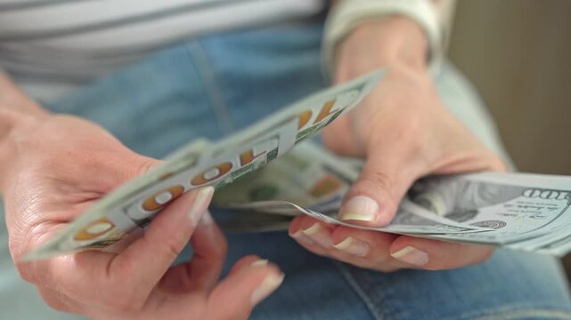 An unidentified woman is sitting and counting dollars. Close-up: the woman&rsquo;s hands are sorting through hundred-dollar notes.