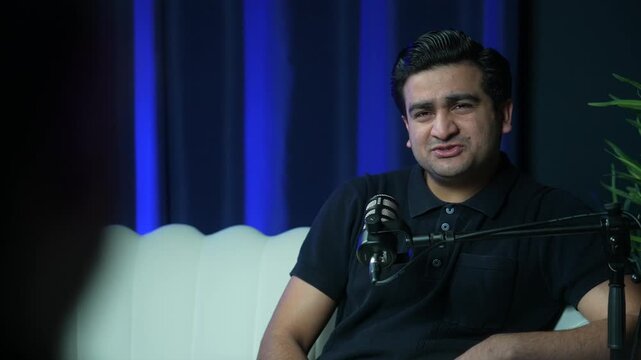 Podcast host gesturing while speaking in modern recording studio, animated pointing back and forth with guest responding gestures