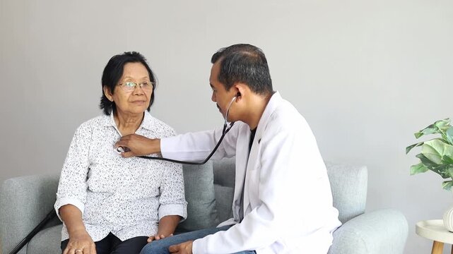 Asian male doctor examining senior woman with stethoscope listening to patient heart beating and lungs through chest