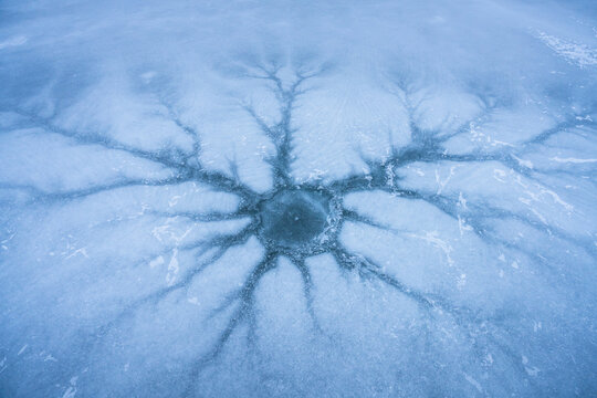 View of intricate dendritic ice patterns radiating from a central hole on a frozen lake surface along the Icefields Parkway in Jasper, Alberta, Canada.