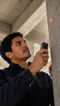 A man focuses on using a laser level tool to measure a concrete wall during construction. Precision and accuracy in building projects.