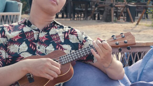 Young man playing ukulele on tropical beach during relaxing summer vacation with peaceful seaside atmosphere