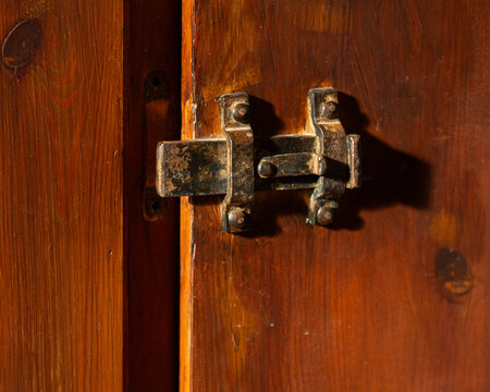 Old iron door bolt lock on an old brown wooden door close-up. The door is ajar