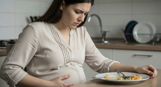 Pregnant woman suffering from morning sickness and nausea looking at a plate of food in the kitchen