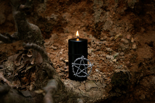 burning magic black candle with pentacle amulet close up on mystery dark abstract nature background. fairy tale scene. witchcraft, practical magic, esoteric ritual. Samhain, Halloween holidays concept