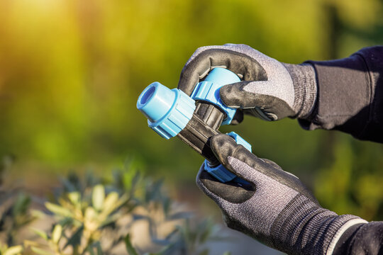 Closeup of hands in the gloves. Process of installing fittings pipes and connectors for the garden and lawn irrigation system installation. Green during sunset, shallow depth of field.
