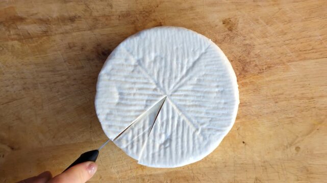 Top view of a person cutting a wheel of traditional white goat cheese on a rustic wooden board, gourmet food preparation and artisan cheese making concept in a Mediterranean kitchen