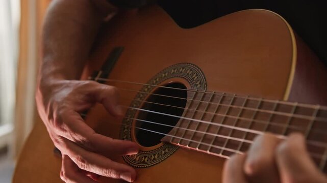 Close up of a person playing music on an acoustic classical guitar, using fingerstyle to shred a solo in slow motion. The musician uses his thumb instead of a pick. The video has beautiful light.