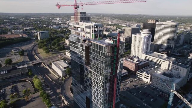 A cinematic high-altitude drone shot orbiting a high-rise building under construction, featuring a large tower crane mounted at the top of the structure. The sweeping aerial movement showcases the sca