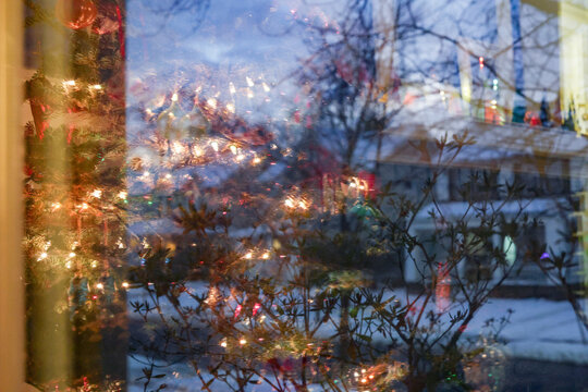 Christmas tree lights reflecting in a window with a snowy outdoor scene visible.
