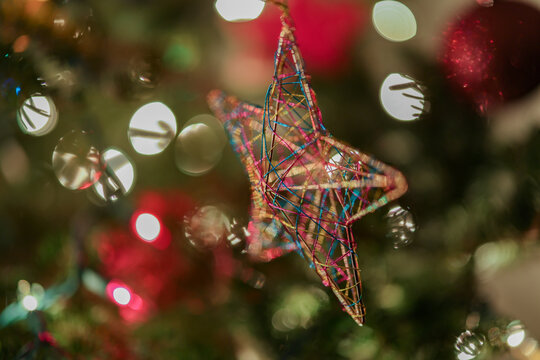 A wire star ornament hangs on a Christmas tree surrounded by colorful bokeh lights.