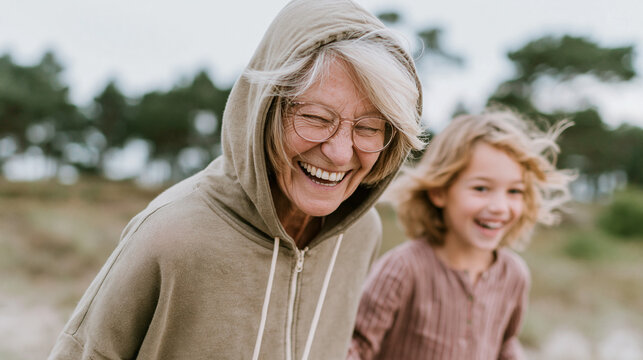Laughing senior and grandchild walking outdoors near trees soft defocused background casual clothing natural unposed movement wide shot intergenerational family outdoor