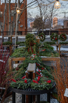 Outdoor market selling Christmas wreaths with festive decorations and city buildings in background.