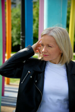 Woman in leather jacket with colorful pillars background, adjusting hair, looking sideways.
