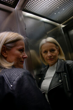 Woman in a leather jacket looking at her reflection in an elevator mirror.