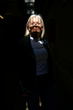 Woman in a dark street with sunlight filtering through stripes on her face.  