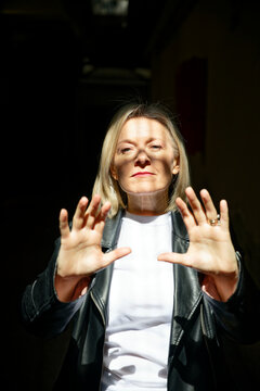 Woman in a black leather jacket reaches toward sunlight with both hands raised.