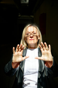 Woman in leather jacket and white top gestures with hands under dramatic lighting.