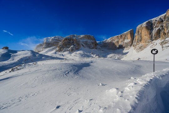 Snowy mountain landscape under a clear blue sky with a sharp, black and white arrow sign.