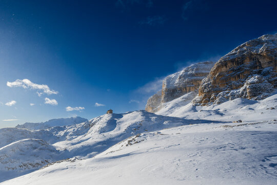 Snow-covered mountains under a clear blue sky with rugged rocky cliffs and drifting clouds.