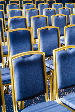 Rows of blue chairs with gold frames in a sunlit empty conference room.