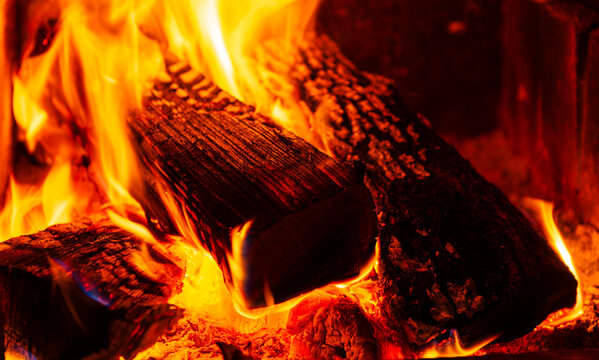 Burning firewood with vibrant flames and glowing embers in a dark setting.  