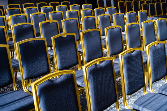 Rows of empty chairs with golden frames in a conference room under bright light.