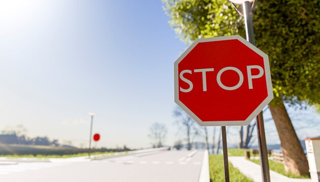 Red octagonal stop sign on a sunny rural road with trees and clear sky.