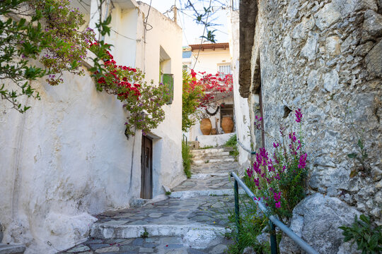 A picturesque, narrow alleyway in the traditional village of Spili, Crete, Greece. In the background, traditional large clay jars (pithoi), enhancing the authentic charm and rustic rural atmosphere