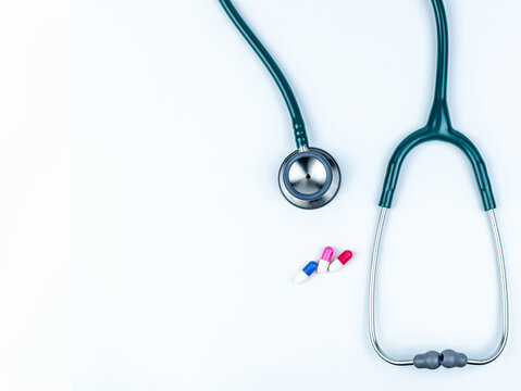 Top view of green stethoscope with pile of antibiotic capsule pills on white table. Antimicrobial drug resistance and overuse. Medical equipment for doctor. Clinical Cardiology. Global Health care.