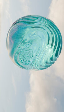 A large, transparent turquoise glass sphere floats against a cloudy blue sky backdrop.