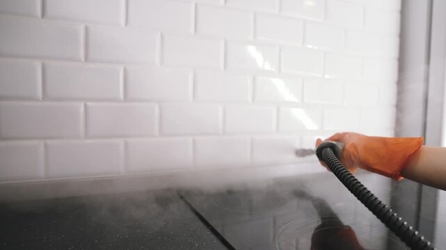 Person cleans white subway tile backsplash and black countertop using a steam cleaner. Focus on hygiene, sanitization, and modern kitchen maintenance. Daily household chore