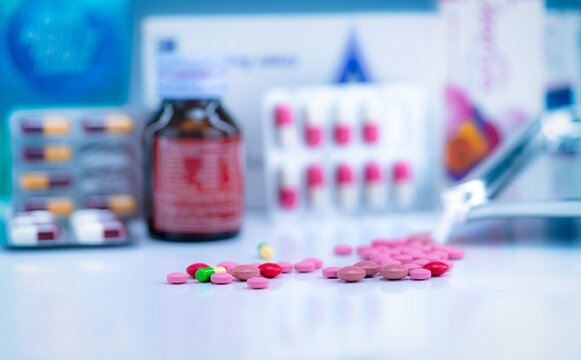 Pile of colorful tablets and capsules pills on blurred drug tray, bottle, and capsule in blister pack. Pharmacy shop background. Healthcare and drug use for treatment illness. Pharmaceutical industry.