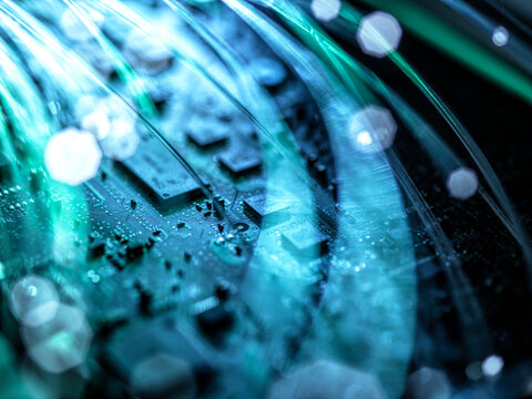 Close-up of a circuit board with glowing fibers and a futuristic blue-green hue.
