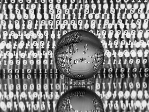 Glass globe with etched continents reflecting on binary code background in black and white.