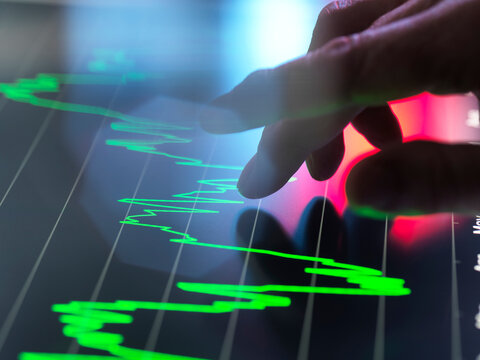 Hand interacts with financial graph on a touchscreen in a high-tech setting.