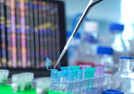 Lab setting with pipette and multicolored test tubes in front of a DNA sequence display.