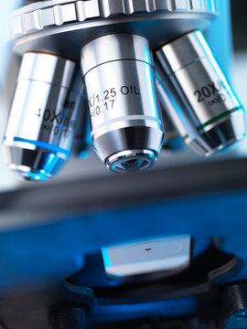 Close-up view of a microscope's objective lenses with a focused light on a slide.