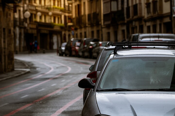 Fototapeta premium Row of cars parked along the street and old buildings in Europe city. Many cars parked on road in old town. City street in Europe. Front view of car parked outside residential building. City traffic.
