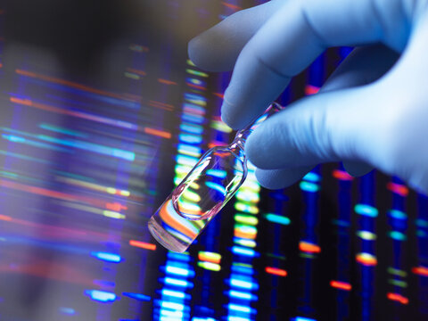 Gloved hand holding vial against colorful DNA sequencing background.