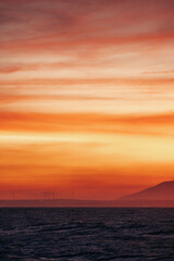Fototapeta premium Stunning sunset over the ocean with distant wind turbines and hills on the horizon. Mui Ne, Vietnam