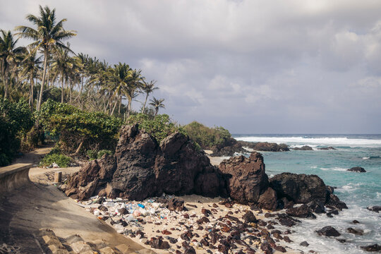 Rocky tropical beach with palm trees, cloudy sky, and turquoise ocean waves. Ly Son island, Vietnam