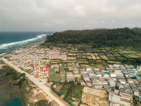 Aerial view of a coastal town with lush fields and ocean waves under a cloudy sky. Ly Son island, Vietnam
