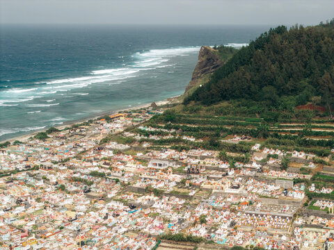 Aerial view of colorful cemetery by the ocean with waves and lush green hills. Ly Son island, Vietnam