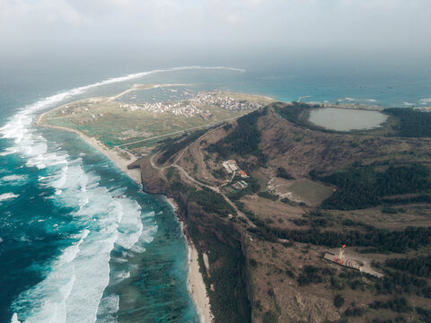 Aerial view of an island with coastal waves, lush vegetation, and small town settlement. Ly Son island, Vietnam